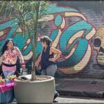graffiti on a wall behind two planters with a woman standing next to it