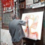 painting on a canvas in a shop window with a man painting