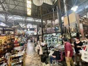 people are shopping in a market with a clock hanging from the ceiling
