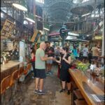 people are standing in a market with tables and chairs