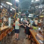 people are standing in a market with tables and chairs