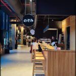 people are walking around a restaurant with a sign hanging from the ceiling