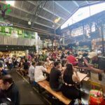 people sitting at tables in a large indoor market area