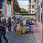 people walking down a cobblestone street with a bus parked in the background