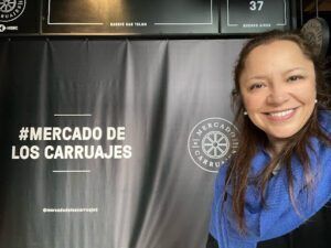 smiling woman in blue scarf standing in front of a sign