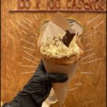 someone holding a pastry in a paper wrapper with a chocolate topping