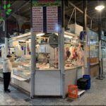 there are people standing in a food market with meat on display