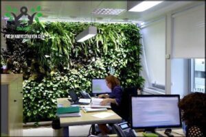 there are two people sitting at a desk with computers and a plant wall