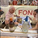 there are two people sitting at a table with a bottle of wine