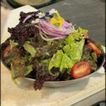 there is a bowl of salad on a counter with a knife