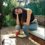 there is a woman sitting on a bench with a drink and a plate of food