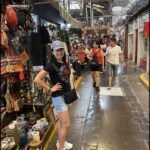 there is a woman standing in a market with a lot of items