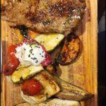 there is a wooden cutting board with a steak and vegetables on it