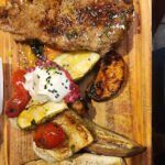 there is a wooden cutting board with a steak and vegetables on it