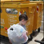 there is a young boy standing next to a yellow dumpster