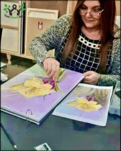 woman sitting at a table with a painting of a yellow flower