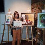 woman standing in front of a painting of a dog holding a certificate