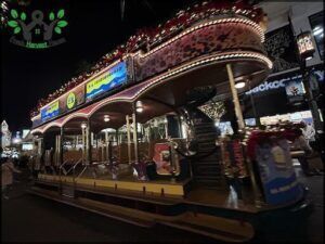 A Christmas-themed trolley car is parked on the street, with its lights on, creating a festive atmosphere.