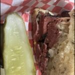 A close up of a sandwich with a pickle on the side.