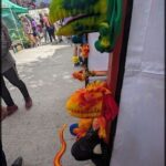 A group of people are standing in front of a display of stuffed animals, including a large green and orange dragon.