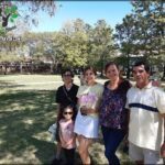 A group of people, including a man, woman, and child, pose for a picture in a park.