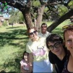 A group of people, including a woman and a man, are posing for a photo under a tree.
