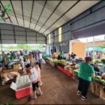 A group of people shopping in a market with a variety of fruits and vegetables.