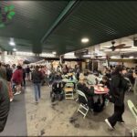 A large group of people are gathered in a crowded room, eating and socializing.