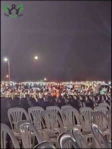 A large group of people are sitting in chairs, looking up at the moon.