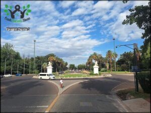 A man is crossing the street in front of a park.
