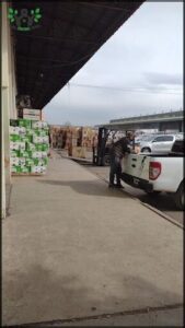 A man is standing next to a white truck, possibly loading or unloading boxes.