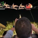 A man is taking a picture of a Christmas display featuring Santa Claus and reindeer.