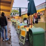 A man walks past a row of tables with umbrellas, some of which are green.