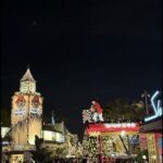 A nighttime scene of a Christmas display with a lit-up Ferris wheel and a lit-up Santa Claus.