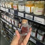 A person holding a bottle of dried red peppers in a grocery store.