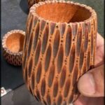 A person is holding a wooden cup with a pattern on it.