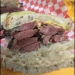 A sandwich with meat and pickles on a red and white checkered paper.