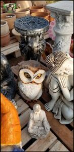 A small owl statue is sitting on a wooden table next to a statue of a monkey.