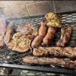 A variety of meats are being cooked on a grill, including sausages and steaks.