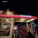 A vintage gas station with a red neon sign and a red car.