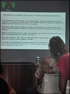 A woman is sitting in front of a screen with a presentation on it.