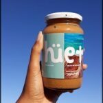 arafed jar of nut butter held up in front of the ocean