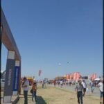 people are flying kites in a field with a blue sky