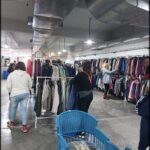 people are shopping in a clothing store with a blue basket