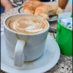 there is a cup of coffee on a plate with a woman sitting in the background