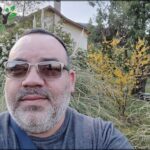 there is a man with a beard and sunglasses standing in front of a house