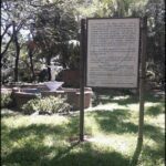 there is a sign that is in the grass near a fountain