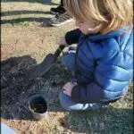 there is a young boy kneeling down with a shovel in his hand