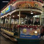 Two men dressed in suits are riding in a trolley car, possibly enjoying a holiday celebration.