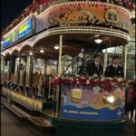 Two men dressed in suits are riding in a trolley car, which is decorated with Christmas lights and a Spongebob theme.